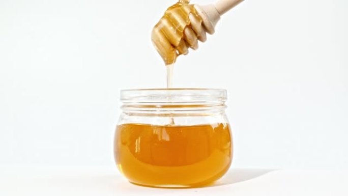 蜂蜜滴，从玻璃碗中的专用蜜勺中倒出。蜂蜜滴在白色背景上。健康食品概念。