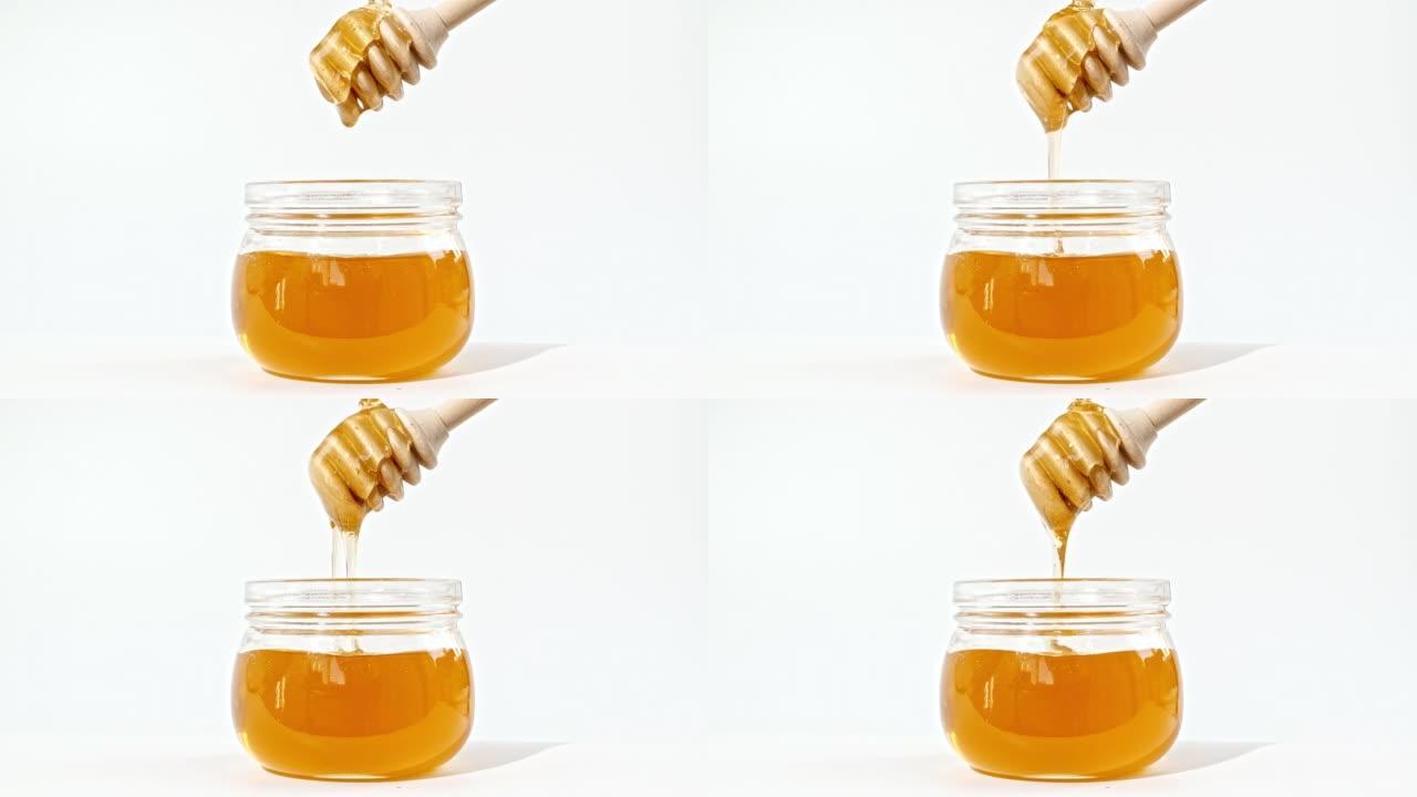 蜂蜜滴，从玻璃碗中的专用蜜勺中倒出。蜂蜜滴在白色背景上。健康食品概念。