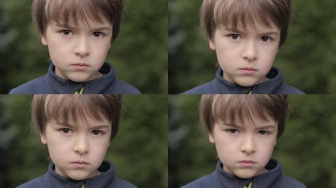 肖像悲伤的小男孩看着相机。思考好奇心的孩子在户外近距离看相机。沮丧的脸眼睛严肃沉思的孩子。童年时消极