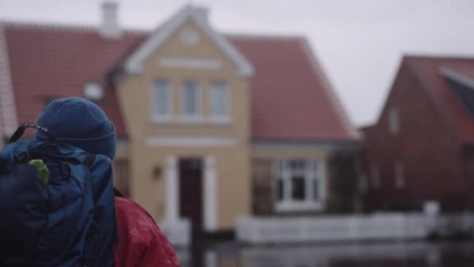 穿着冬装的背包的男人在雨中走在潮湿的柏油路上