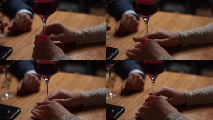 晚上在高档餐厅与优雅的男人浪漫约会时，无法辨认的女人紧张地用红酒抚摸着玻璃脚的特写手。