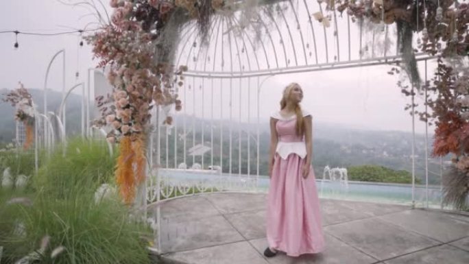一位穿着粉红色连衣裙的公主在花园里的笼子里玩耍，鲜花环绕着她