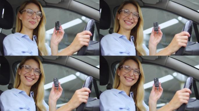 穿着时尚眼镜的兴奋积极的女人拿着和展示汽车钥匙坐在新豪华车的驾驶座上，享受内饰和快速送货服务的女士，