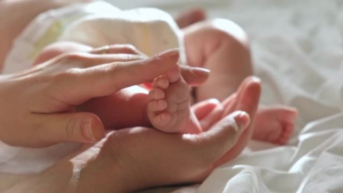 婴儿的脚在母亲的手中，在她的手掌上。快乐的父母抱着婴儿的脚，特写。生育，家庭，生育概念。女人触摸婴儿