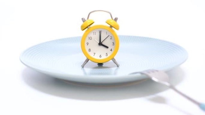 白色背景的空盘子上有闹钟和叉子，间歇性禁食的概念。