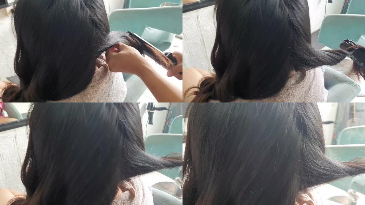 在理发店使用直发器卷曲女性头发的特写