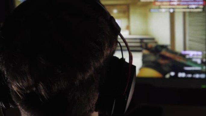 一个男孩在黑暗的房间里玩电脑游戏的特写镜头。戴着耳机。