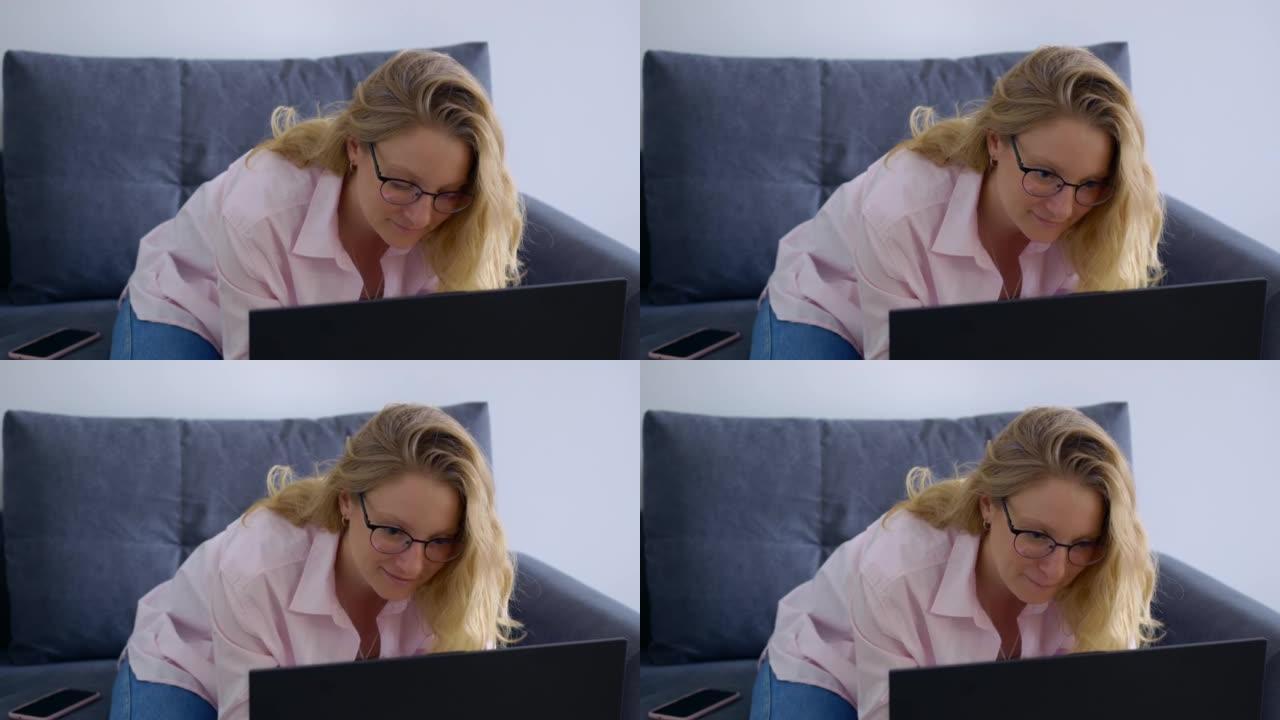 金发碧眼的美女微笑着在家中的笔记本电脑工作。在家远程工作，不用去办公室。简化工作并降低成本互联网上最