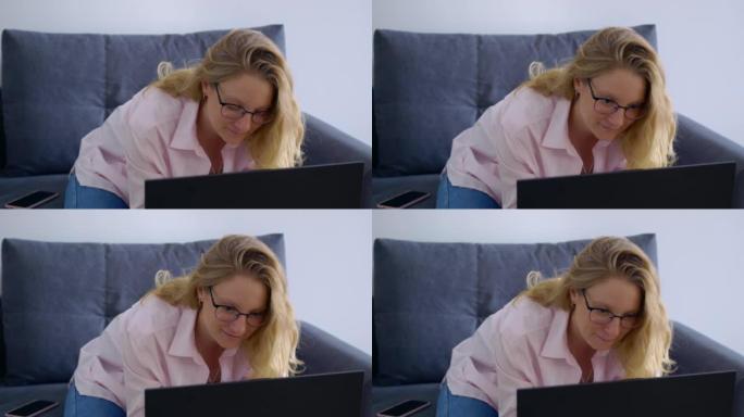 金发碧眼的美女微笑着在家中的笔记本电脑工作。在家远程工作，不用去办公室。简化工作并降低成本互联网上最
