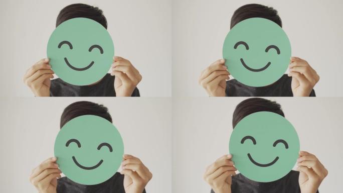少年手持绿色快乐笑脸剪纸，心理健康评估，儿童积极健康，世界心理卫生日概念