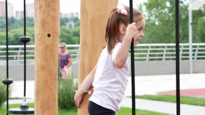 一个快乐的小女孩正在用木头制成的现代运动场上攀登障碍赛