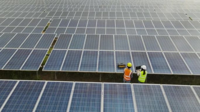 鸟瞰图技术工程师走过太阳能电池板，在太阳能农场检查太阳能电池板。