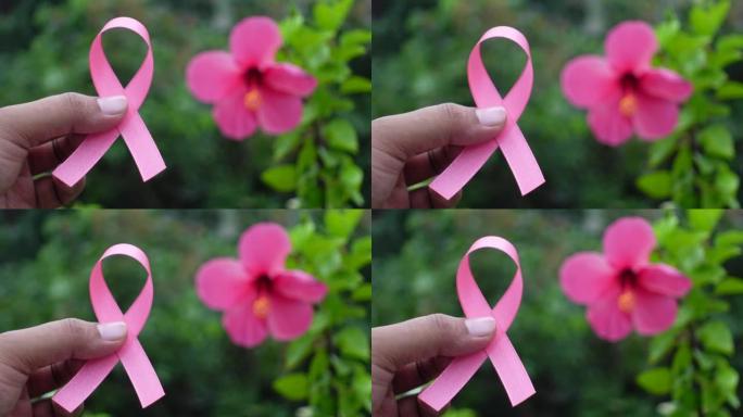 粉色丝带乳腺癌意识图标徽章在花和绿叶背景上的手指上举行。世界癌症日，10月粉红日，全国癌症幸存者日概