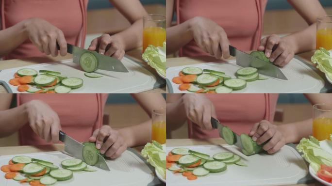 女人的手在厨房的砧板上握着刀并切成黄瓜的特写