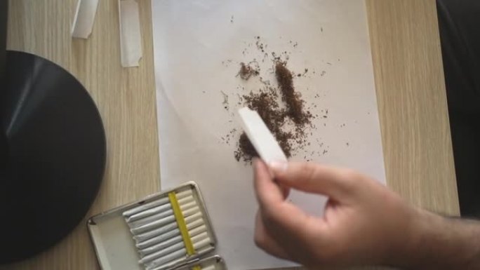 男性将香烟过滤嘴放在卷纸中并定位