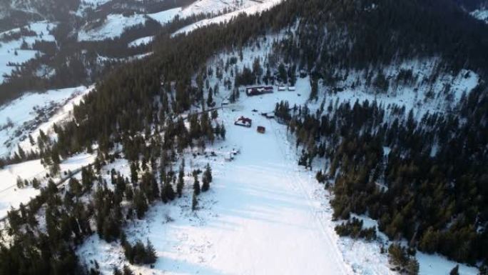 鸟瞰图。飞越冰冷的松树林，驶向冬季度假胜地和滑雪场。雪上滑雪跟踪冬日升起在安静的滑雪胜地上方