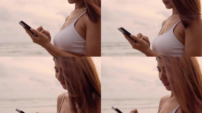 年轻的亚洲妇女使用智能手机，度假时在海滩上散步，使用电话进行交流。
