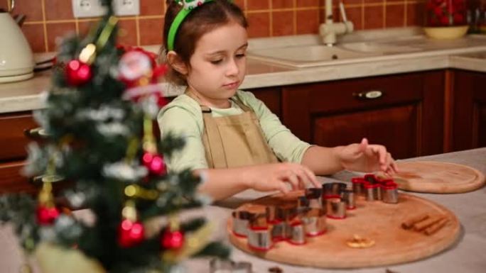 观看圣诞树，并在家庭厨房里一个拿着姜饼切刀的漂亮的孩子女孩身上改变焦点