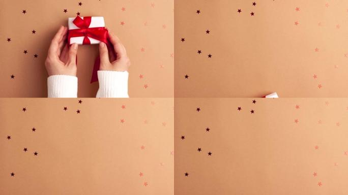 穿着白色毛衣的人的手拿走了一份白纸礼物，上面有一个红色缎带蝴蝶结，棕色背景是红色星星。定格动画圣诞假