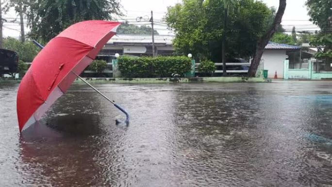 低角度看雨水倾泻美丽的红色雨伞，留在铺好的道路上。