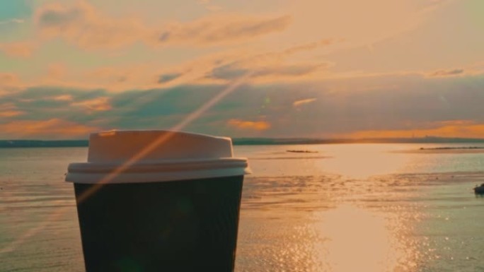 日落时在路堤长椅上的纸杯里喝咖啡