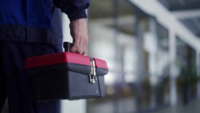 人携带工具箱和万用表测试仪。电工去修理办公室的灯。主人完成电力工作。穿着制服的男机械师。