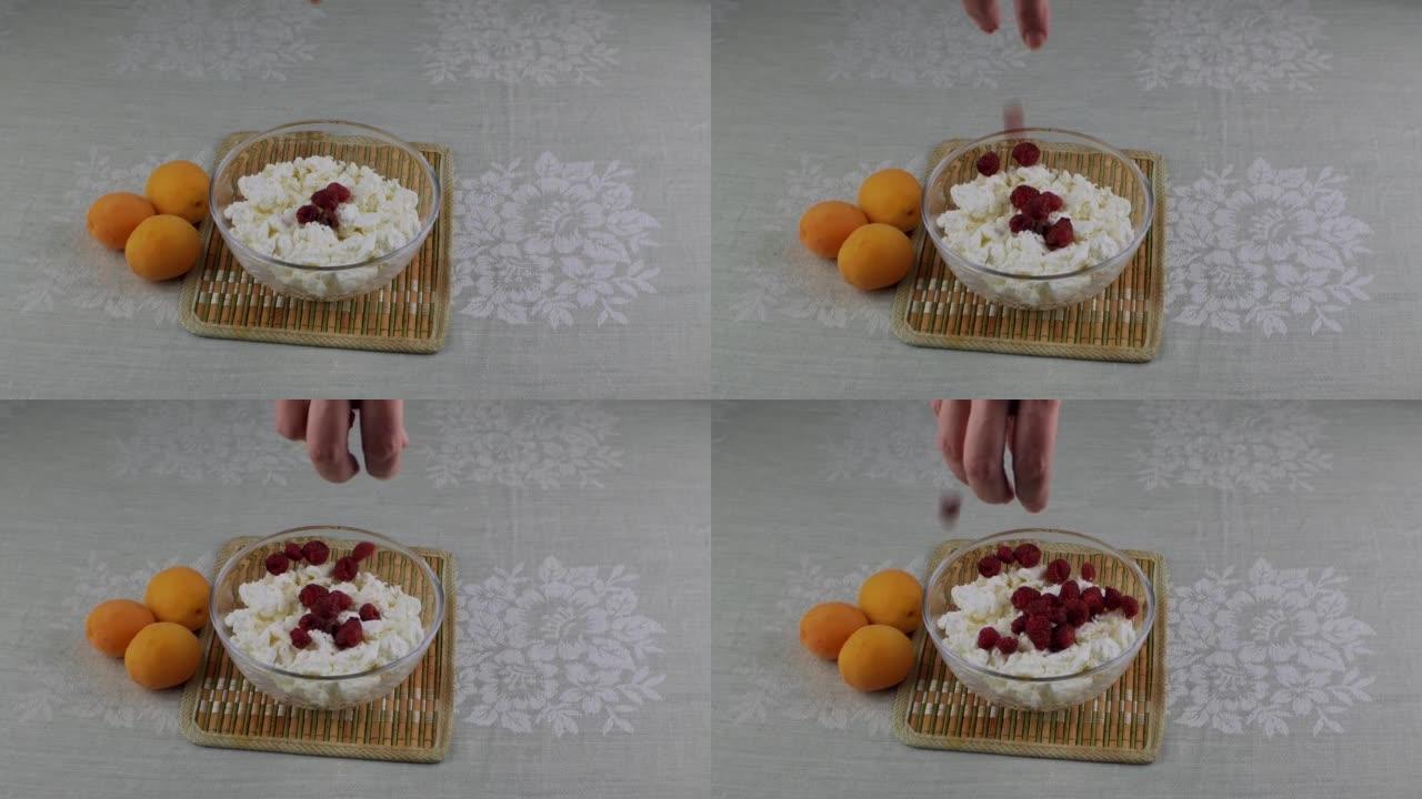 一个女人的手把红树莓扔进一碗奶酪里。