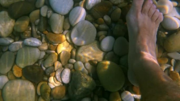 在石质海床上有阳光反射的水下行走的人脚和腿的第一人称fpv视图