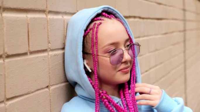 一个高加索青少年时髦女孩的肖像，粉红色的辫子靠在粉红色的砖墙上。Z世代风格。