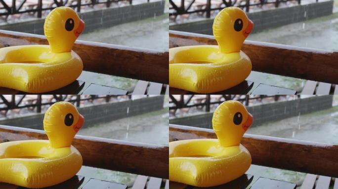 一只充气鸭子躺在娱乐中心凉亭的木桌上，在游泳池被雨水覆盖的背景下