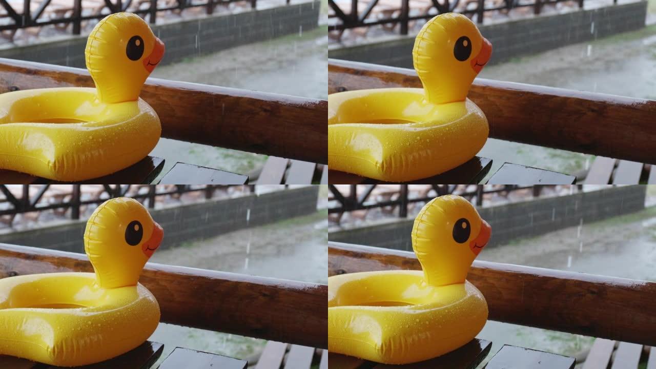 一只充气鸭子躺在娱乐中心凉亭的木桌上，在游泳池被雨水覆盖的背景下