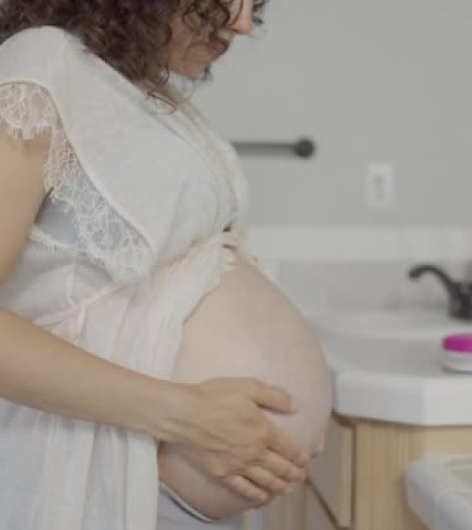 一个怀孕的三十多岁的民族妇女在浴室里在怀孕的肚子上擦乳液的垂直视频