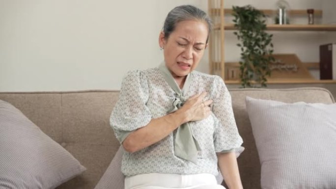 成熟的亚洲女人心脏病发作，坐在沙发上。
