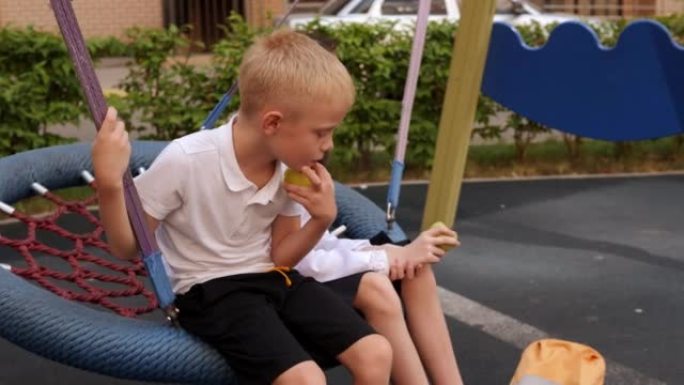 两个孩子放学后坐在圆秋千上吃苹果。