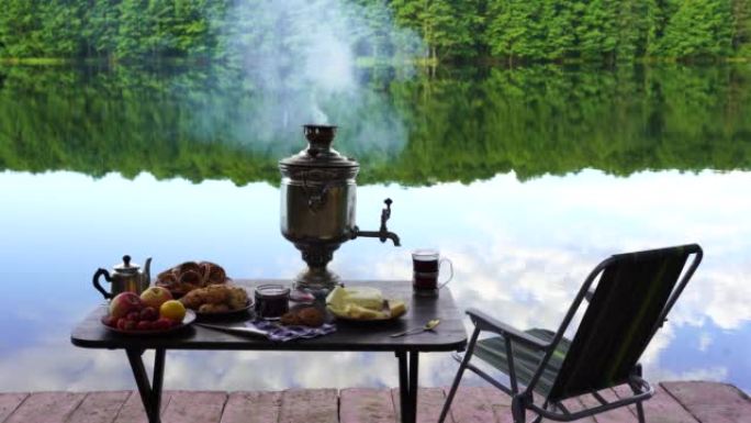 复古金属茶茶炊，白烟和食物在湖边的桌子上