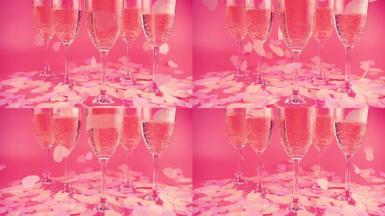 在粉红色的背景上带有起泡酒的玻璃杯，并带有心形的五彩纸屑。慢动作。