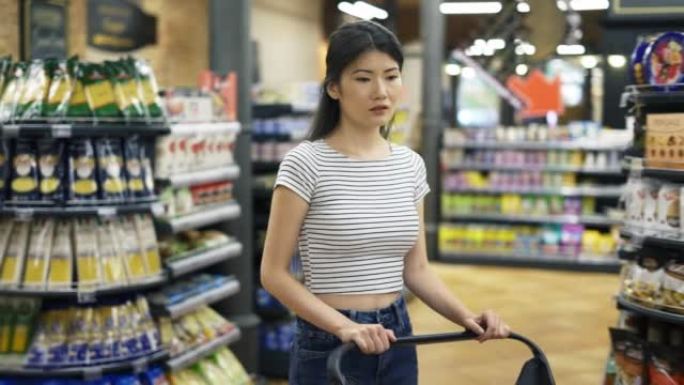 快乐的亚洲女孩带着购物车在超市里走来走去。购物之旅。日常业务