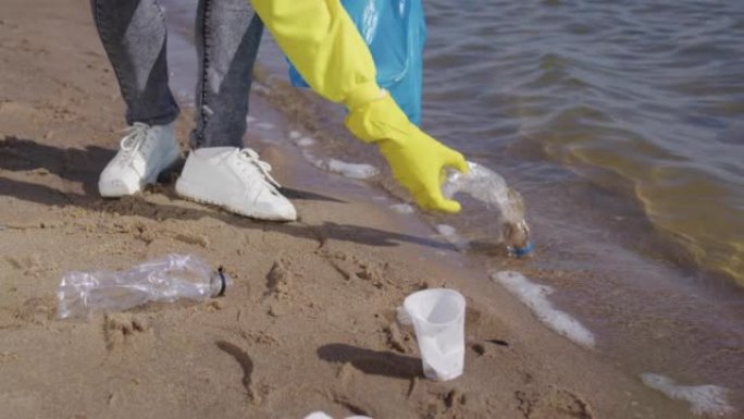女人捡起散落在沙子上的塑料袋和瓶子