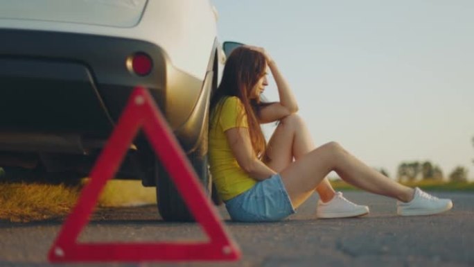 Young upset girl sitting next to broken car on sid