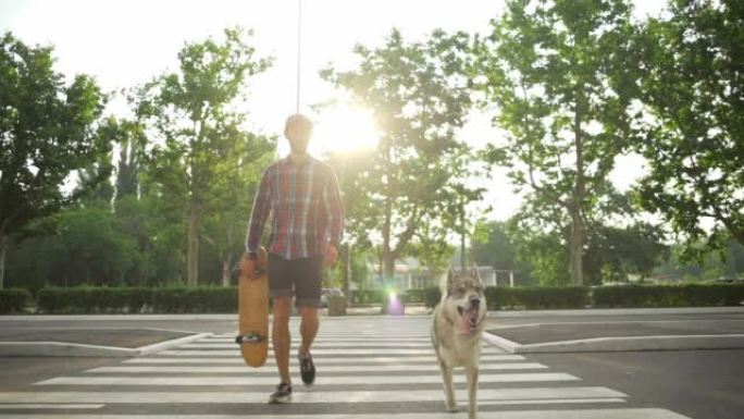 小男孩带着哈士奇狗带着滑板行走阳光路慢动作快速