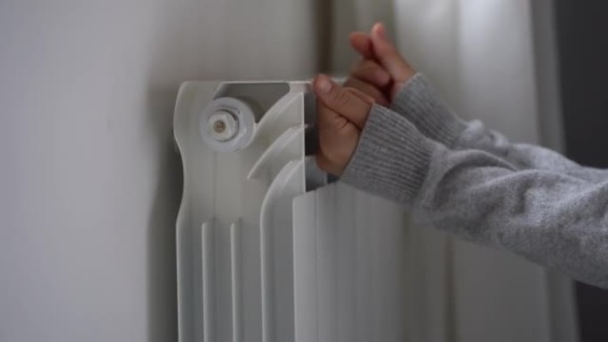 女人变冷，试图感受温暖，把手放在运动衫里，放在公寓里的暖气片上