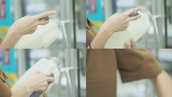 戴着口罩的亚洲妇女在超市用智能手机买牛奶