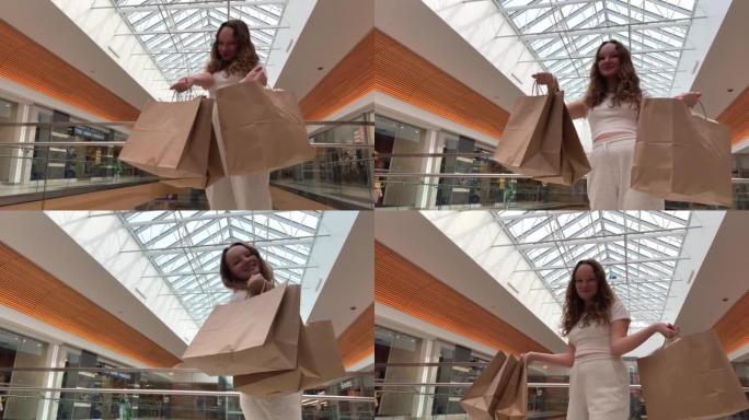 年轻的少女展示包裹她有了新的购买，她刚刚在一家大商店买东西，她在透明的屋顶上穿着白色衣服旋转和跳舞