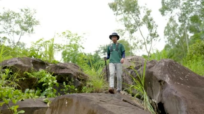 4K，亚洲男性徒步旅行者爬山，用他们的包和跟踪民意调查欣赏大自然。周末还喜欢从大石头上爬山，丛林漫步