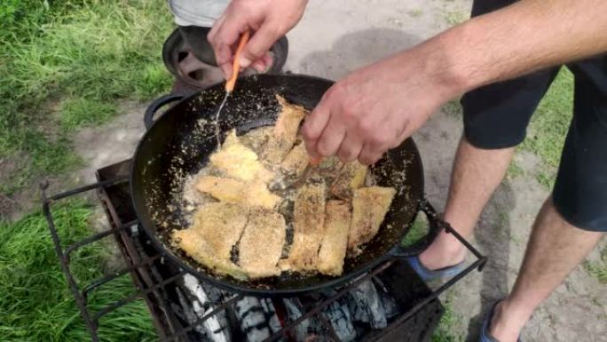 在着火的锅里烤长矛。小脆皮鱼片在油中油炸。自然界烹饪食物的概念。一个人准备食物，然后用抹刀翻转。浅景