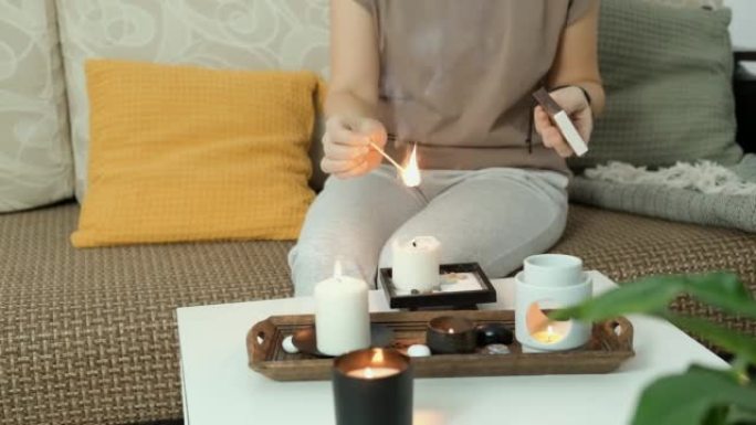 女人坐在家里的沙发上，点燃香薰蜡烛。舒适的家庭芳香疗法和放松，抗压力和整体休息。精神卫生概念。