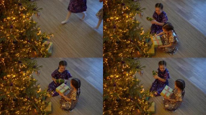 两个兴奋的女孩坐在地板上的圣诞树下拿着礼品盒