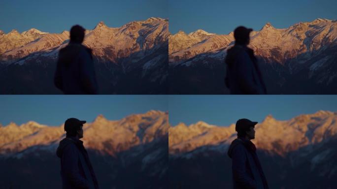 在印度喜马al尔邦的马纳利，一名印度男子在日落时凝视着白雪覆盖的山脉。焦点从白雪覆盖的山脉到前面的人