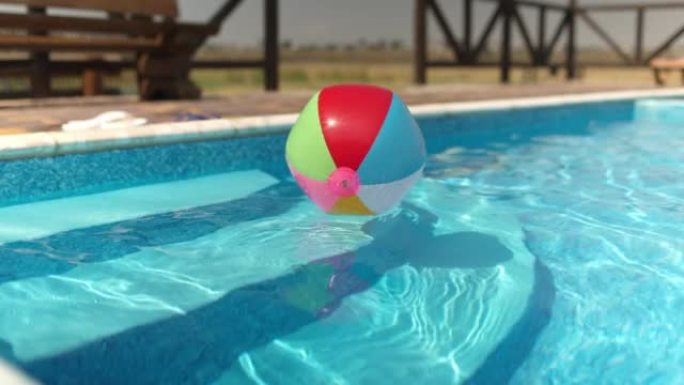 在夏日的阳光下，一个充气球漂浮在碧水的蓝色水池上