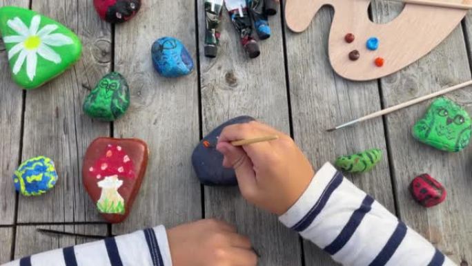 一个孩子的手用丙烯酸颜料在石头上画真菌的镜头。家庭爱好是真实的。